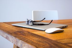Closed laptop with reading glasses and a mouse on a wooden desk