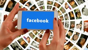 Hands holding a phone showing Facebook against a fan of profile photographs