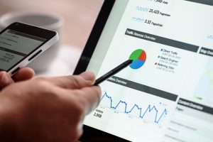 Hand using a stylus on a tablet showing analytics charts beside a phone