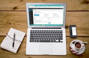 Laptop showing a WordPress dashboard beside a notebook and a coffee cup