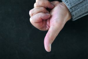 Hand making a thumbs-down gesture against a dark background