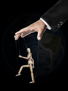 Hand controlling a wooden artist's mannequin on strings against a globe