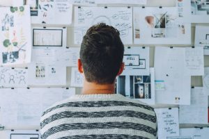 Man seen from behind studying a wall covered with notes and sketches