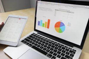 Laptop displaying bar and pie charts beside a tablet on a desk