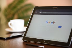 Tablet on a desk showing the Google search page beside a coffee cup