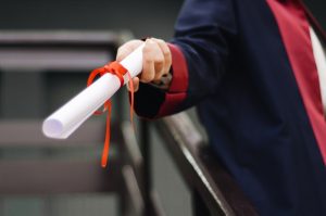 Hand holding a rolled diploma tied with a ribbon