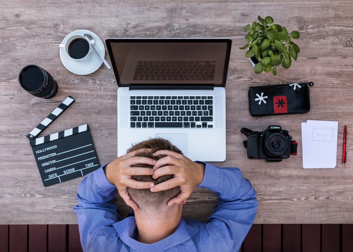 man holds head in front of macbook