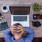 man holds head in front of macbook