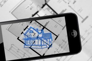 Smartphone displaying a 3D house model held over architectural blueprints