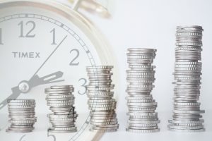Stacks of coins rising in height beside an analogue clock