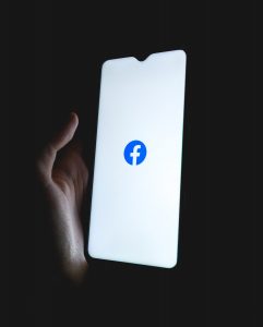 Hand holding a phone in the dark displaying the Facebook logo