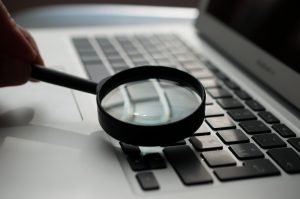 Hand holding a magnifying glass over a laptop keyboard